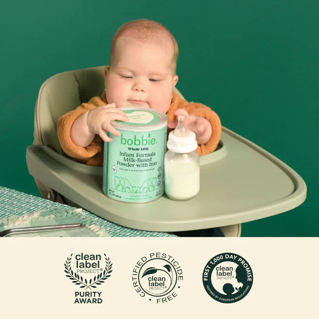 Baby in a high chair with a container of Bobbie Whole Milk Powder and a bottle, against a green background.