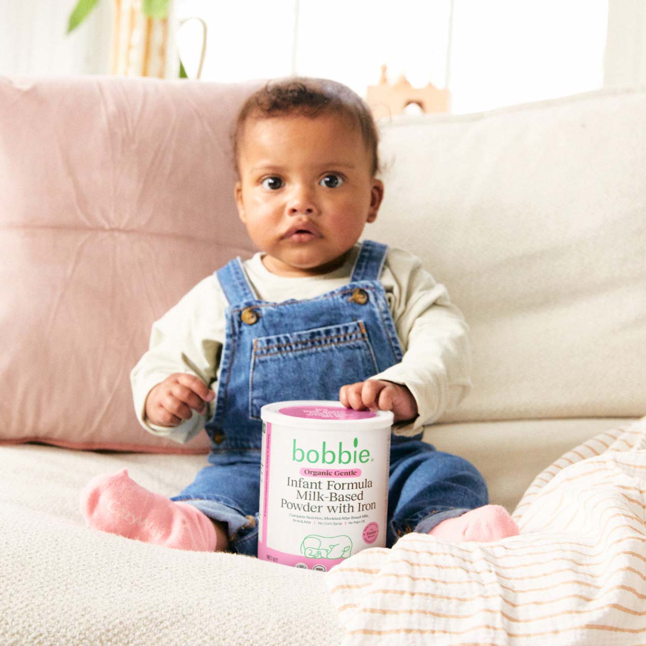 Lifestyle image of a baby sitting with a can of Bobbie Organic Gentle Infant Formula