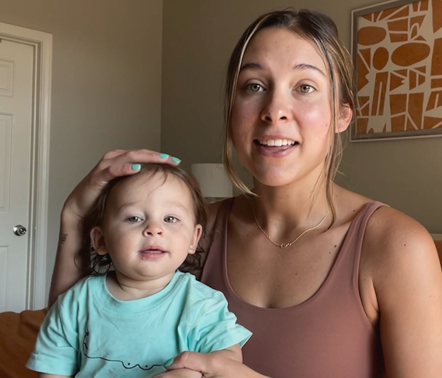 Mom's hand rests on baby boy's head, both looking at the camera