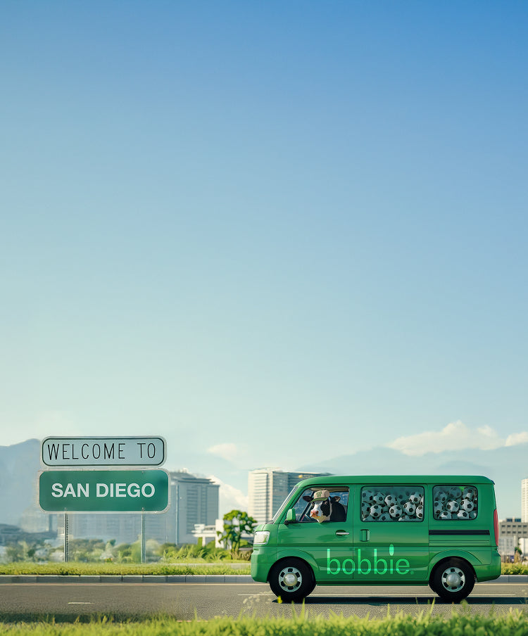 Cow driving a Bobbie car filled with soccer balls